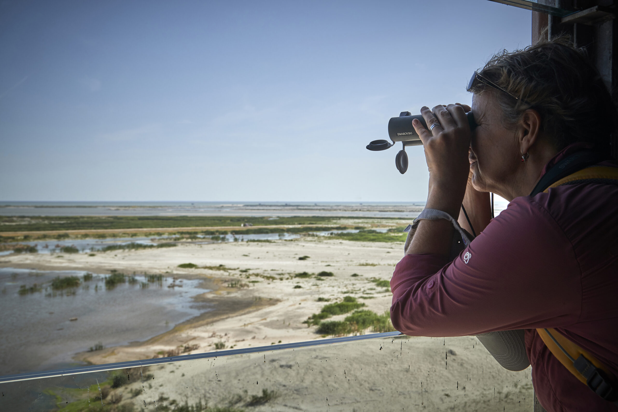 Vrouw kijkt met verrekijker richting Marker wadden.